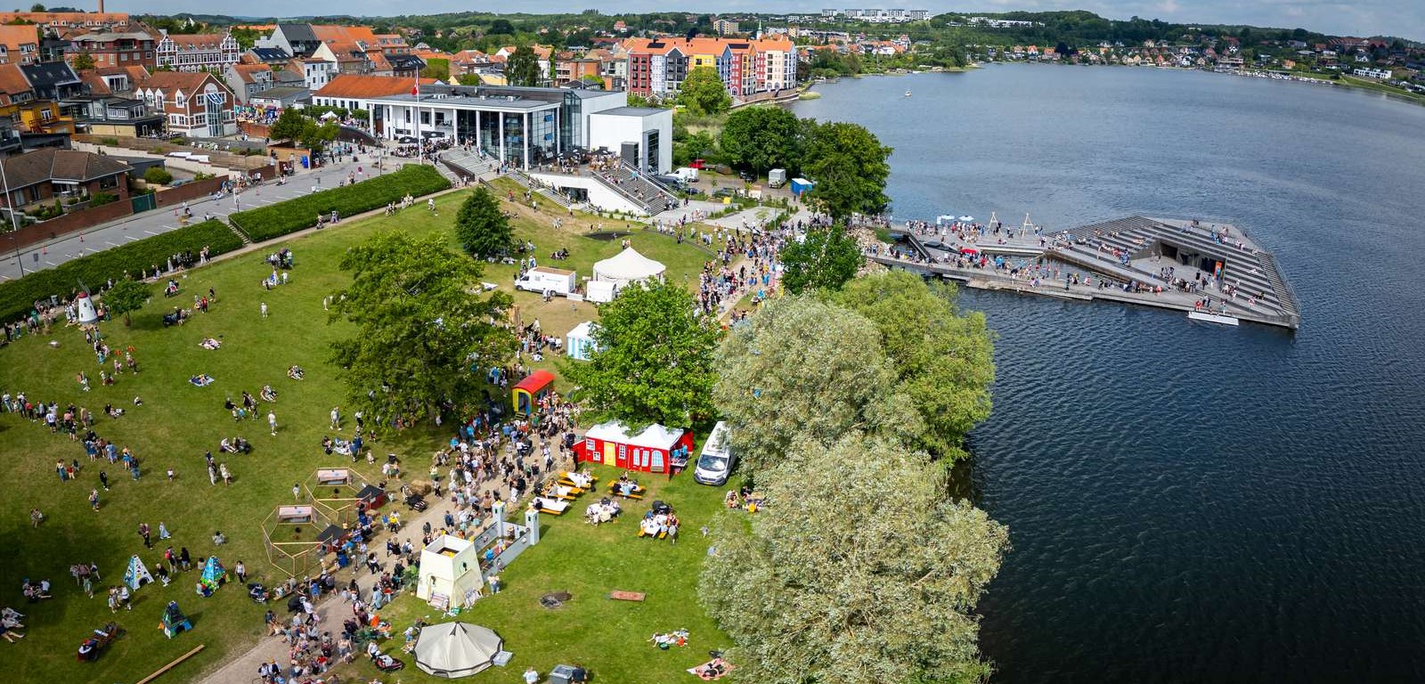 Dronefoto af Sløngeldagene i Skanderborg med mylder af mennesker i Byparken og ved Bybadet. Kulturhuset og byen er i baggrunden.
